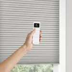 Motorized honeycomb shade with hand showing remote.