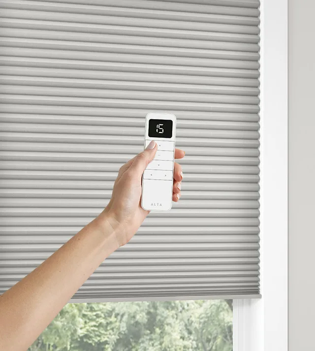 Motorized honeycomb shade with hand showing remote.