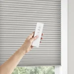Somfy motorized honeycomb shade with hand showing remote.
