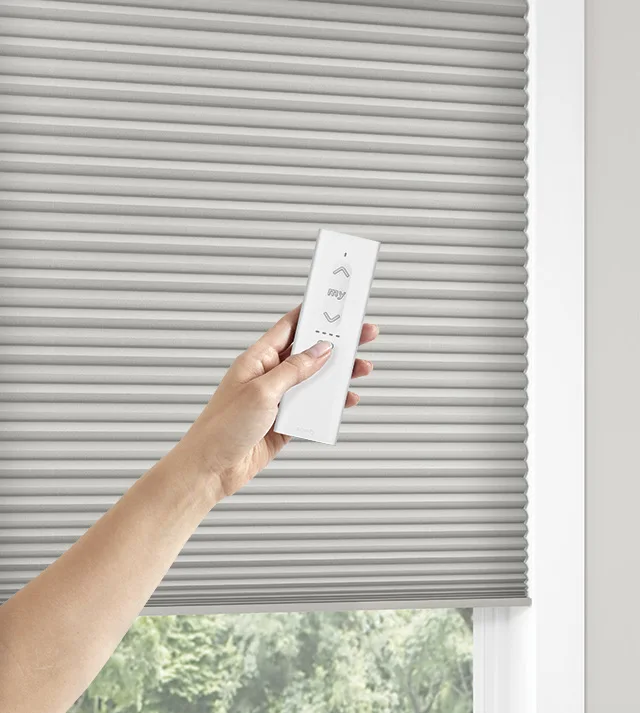 Somfy motorized honeycomb shade with hand showing remote.