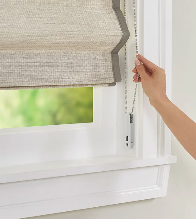 Natural woven shade with a continuous loop bead chain system, featuring a child-safe tensioner, showcased on a display in a Nicholasville, KY showroom, framed by sleek wooden trim and soft spotlighting.
